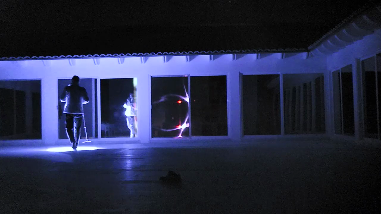 A blue-lit courtyard at night, with figures seen through glass doors
